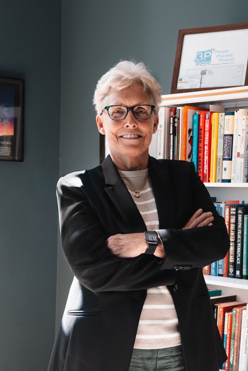 Media kit headshot of Debra Shumar standing arms-crossed in her home office.